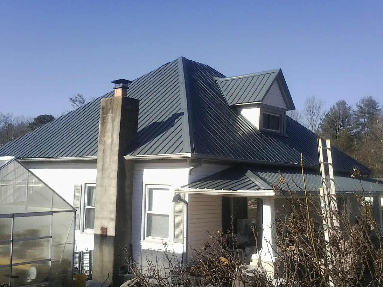 Dark blue standing seam metal roof on a white farmhouse with dormer — Slate & Tile Roof Repair by Roofing Brothers in Sanger
