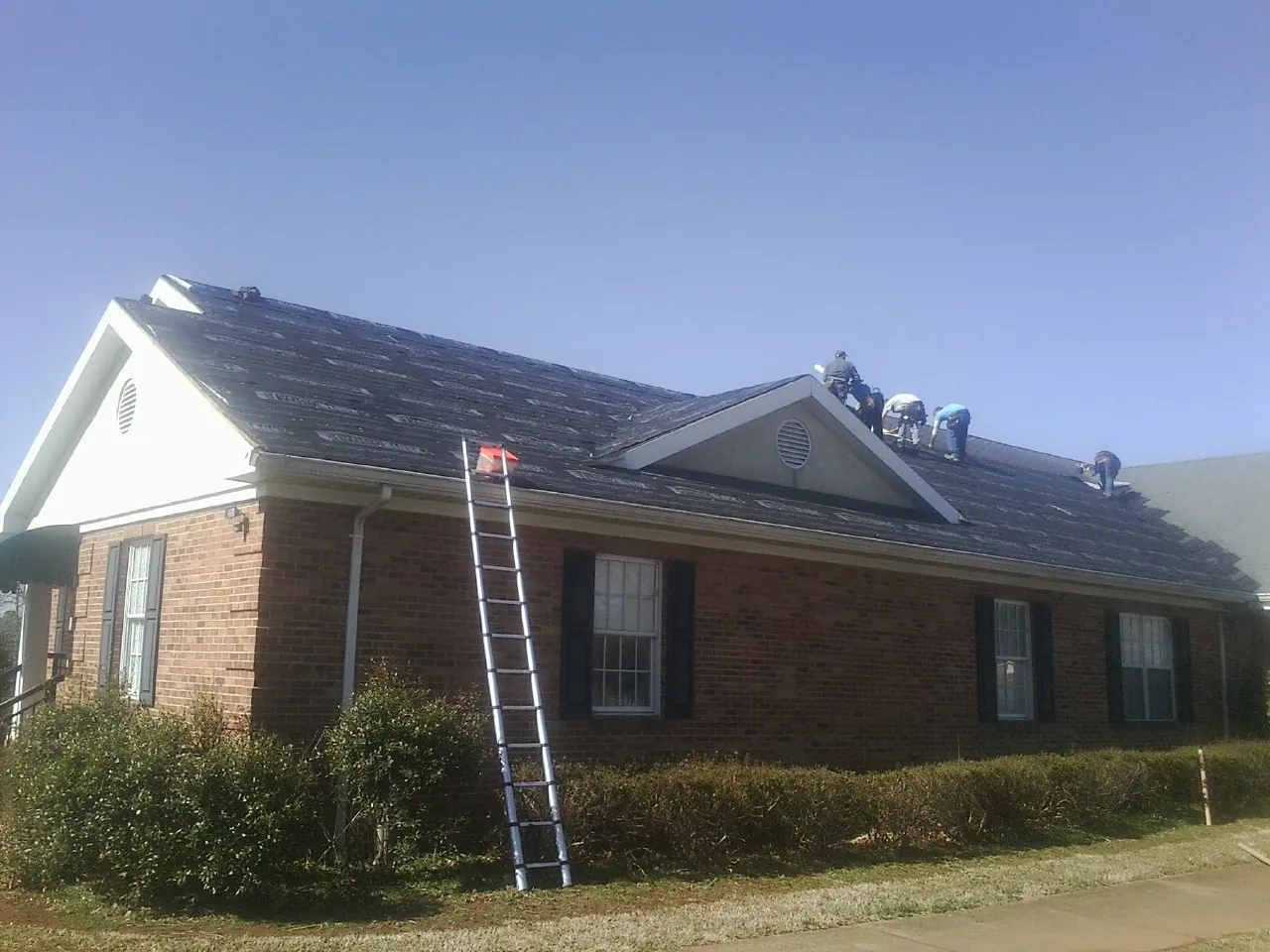 Crew tearing shingles off a brick ranch roof with a ladder set — Emergency Roof Repair work by our crew in Sanger
