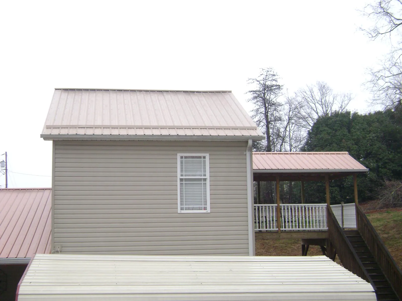 Tan metal roofs on a two story addition and attached porch, from a Roof Replacement job in Sanger